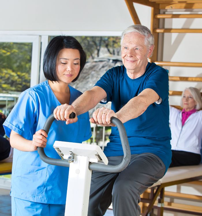 A man in blue shirt is on stationed bike with a woman in blue scrub standing beside him.