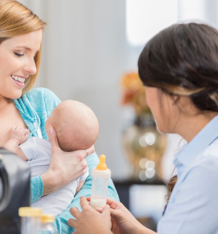 A woman is holding the baby's bottle while another woman in green shirt is holding the baby.