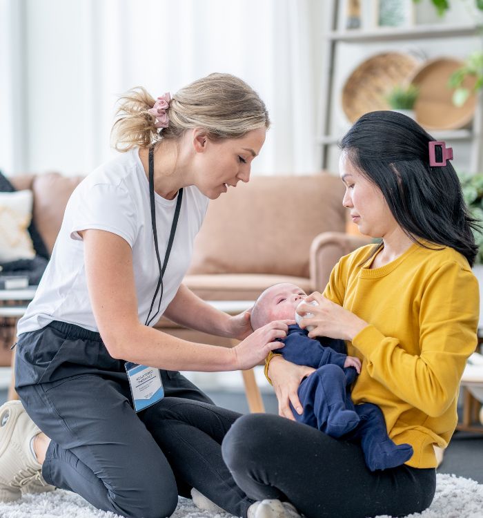 A woman in yellow is holding a baby while the woman in a white shirt is kneeling beside her.
