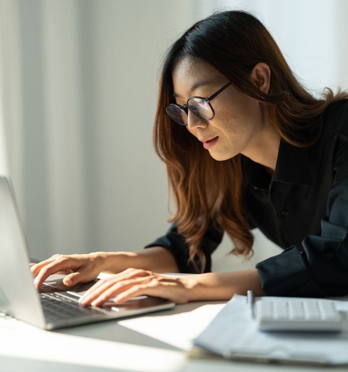 A woman wearing glasses and a black shirt is typing on a laptop.