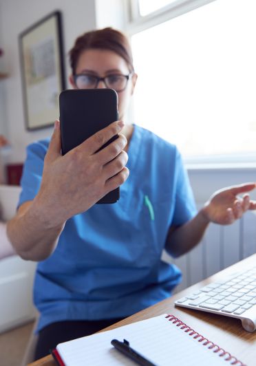 A woman in a blue shirt holding a black cell phone.