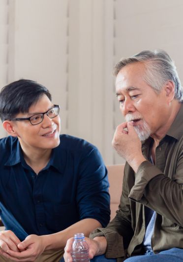 Two men sitting down, one wearing glasses and a blue shirt.