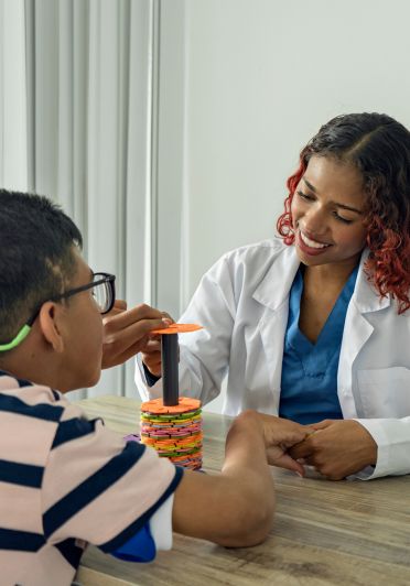 A woman in a white lab coat is smiling at a boy.
