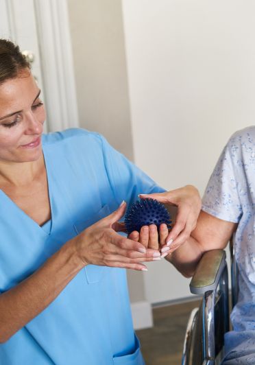 A woman in a blue shirt is helping a patient hold a blue ball.