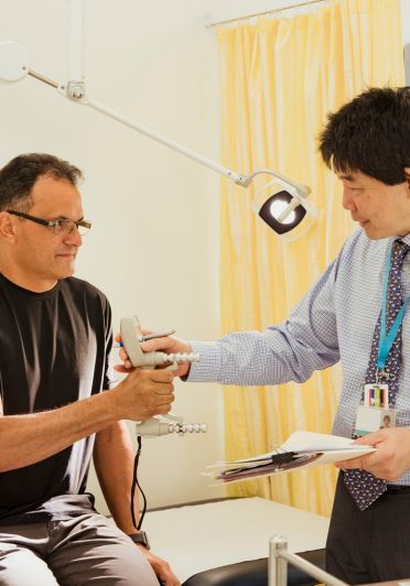 A man in a black shirt is holding a device in front of a man in a blue shirt.