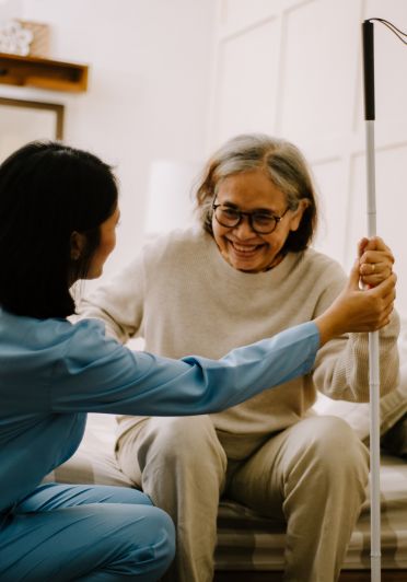 A woman in a blue srub is assisting an elderly woman sitting on a bed.