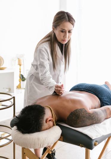 A woman in a white coat giving a man lying on table a back massage.