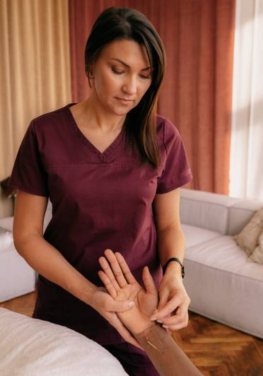 A woman wearing a maroon shirt is performing acupuncture on a patient's hand.