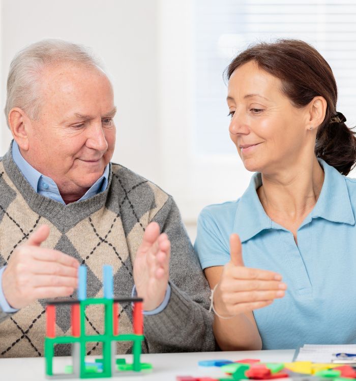 A woman and an elderly man joyfully playing together with colorful toys on a bright, cheerful surface.