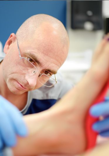 A man with glasses receives a foot examination from a medical practitioner.