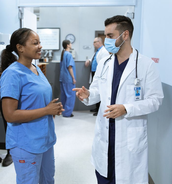 A doctor and a nurse converse in a hospital hallway.