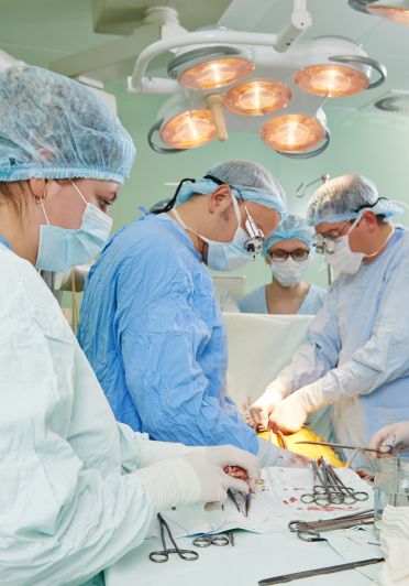 A team of medical professionals in surgical attire performing a procedure on a patient in an operating room.