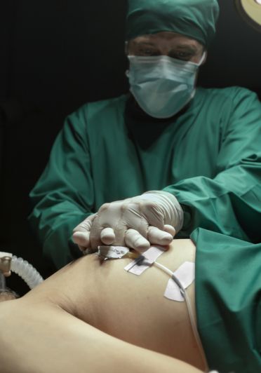 A surgeon in scrubs with his hands on a patient.