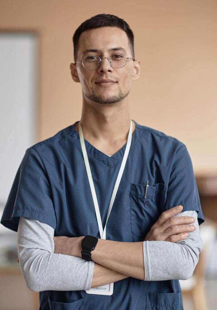 Male doctor standing in his office, dressed in a blue scrub. 