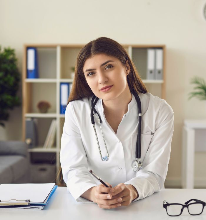 A female doctor seated at a desk, wearing a stethoscope.