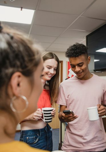 A group of three young individuals gathers around a table, enjoying coffee and discussing together.