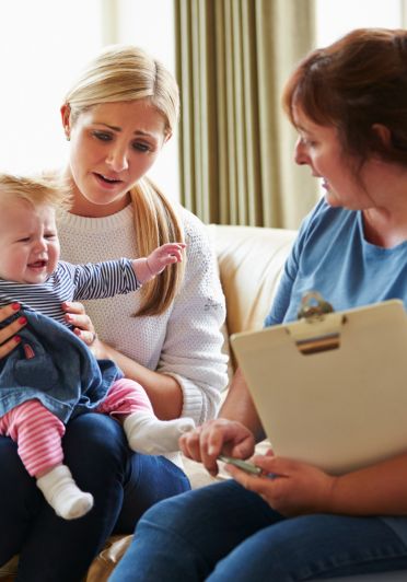 A woman holds a baby while conversing with another women in a warm, friendly setting.