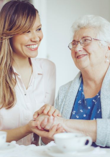 A younger woman gently holding hands with an older woman.