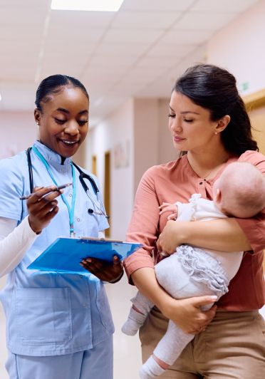 A nurse engages in conversation with a woman holding a baby.