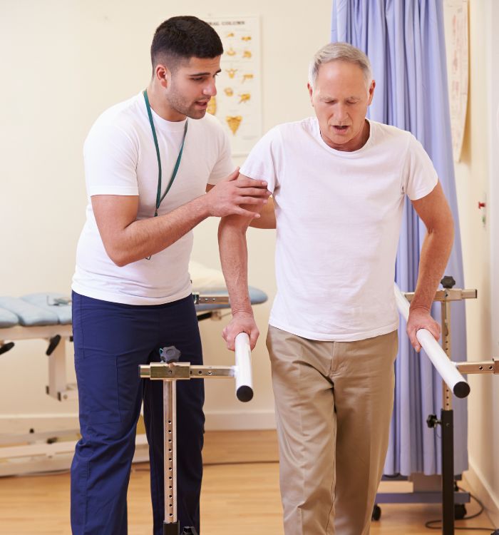 A younger man supports an older man to walk, helping him move safely and confidently.