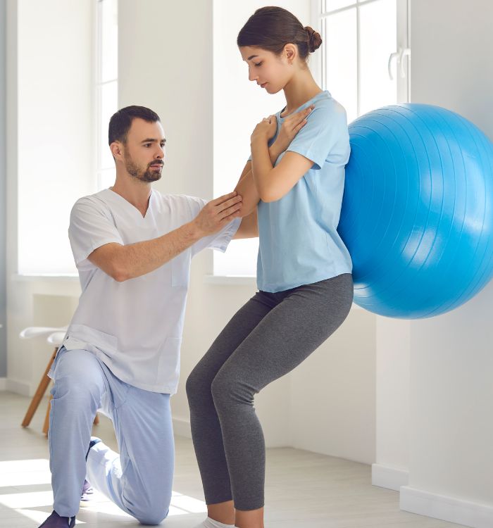 A man and woman perform physical therapy exercises together in a bright, spacious therapy room.