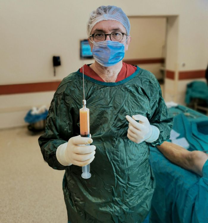 A man in a surgical gown holds a syringe, preparing for a medical procedure.