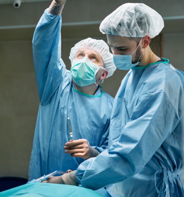 Two surgeons in blue scrubs and surgical masks stand together in an operating room.