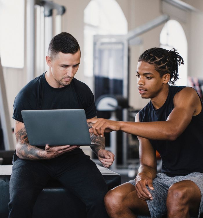 Two men in a gym, one of them is using a laptop.