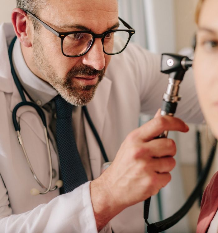 A man in a white lab coat is checking a woman's ear.