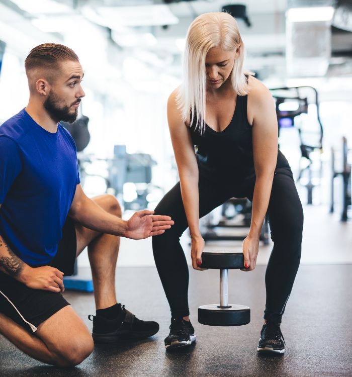 A man kneeling down next to a woman who is lifting a weight.