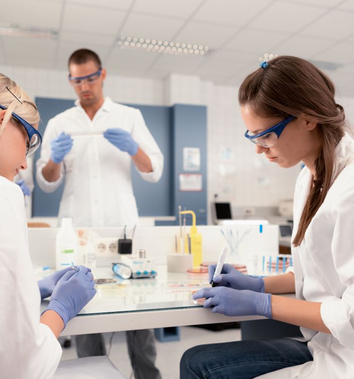 Two women wearing lab coats and safety gloves working on a project.