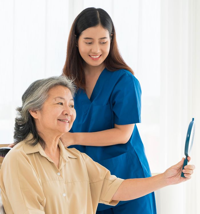 A woman with a blue shirt and a woman with a brown shirt are standing in front of a mirror.