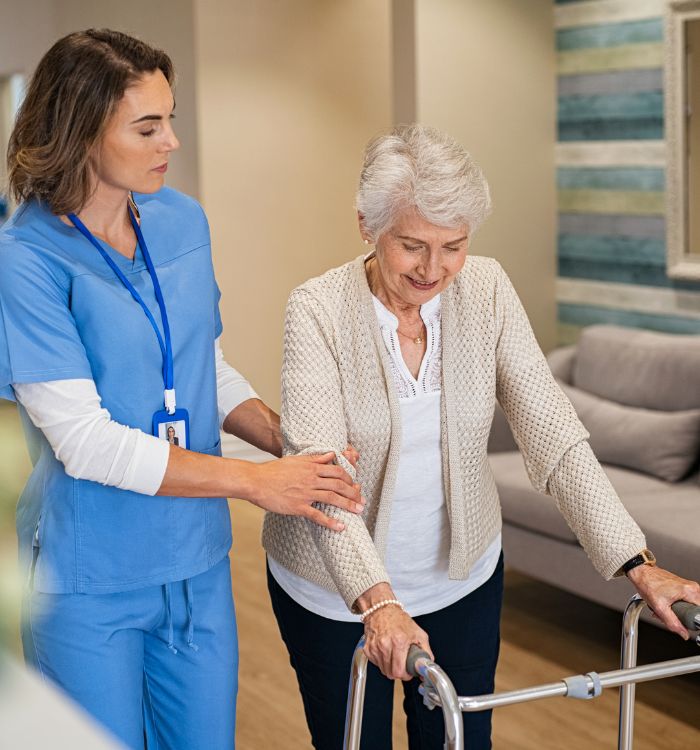 A woman in a blue shirt is helping an elderly woman with her walker.