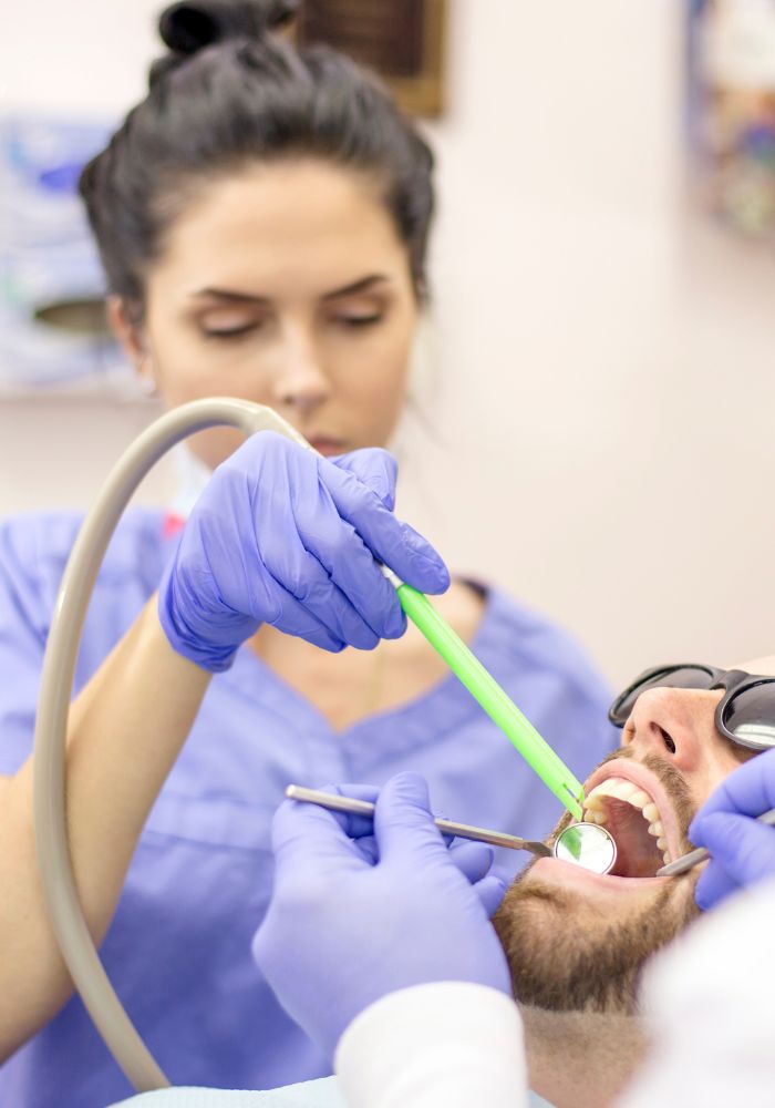 A woman in a blue shirt is holding a suction machine to a man's mouth.