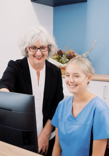 A woman in a blue shirt is smiling at a computer screen.