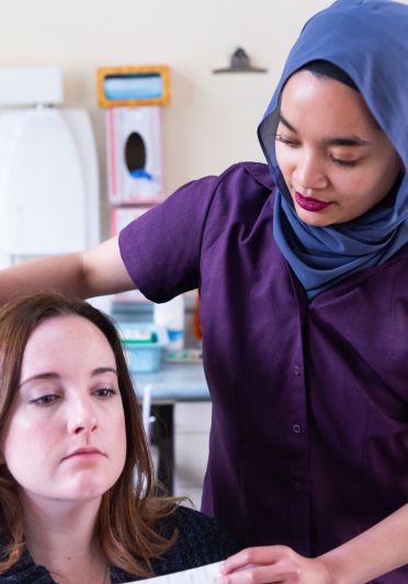A woman with a purple shirt and a head scarf is cutting a woman's hair.