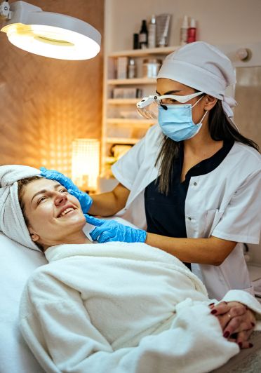 A woman is getting her face waxed by a woman in a white lab coat.