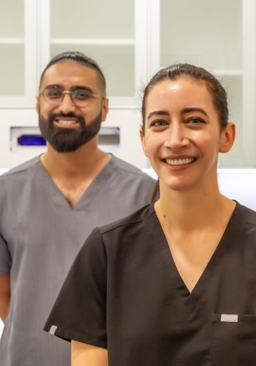 A man and woman in scrubs standing in front of a white wall.