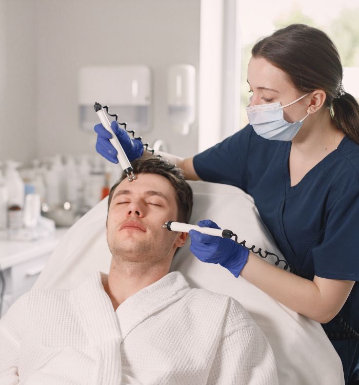 A woman is using a machine to give a man a facial treatment.