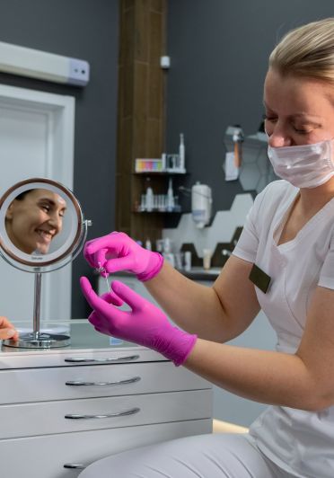 A woman wearing a white shirt and pink gloves is looking something through a mirror.