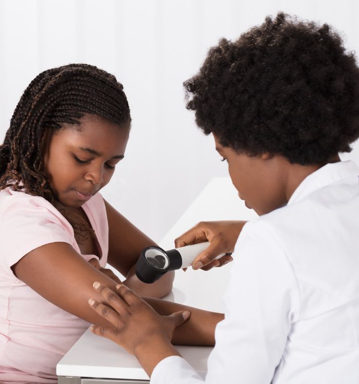 A woman with a pink shirt is getting her skin checked by a woman in a white shirt.