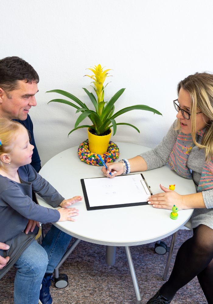 A woman having a discussion with father and child at a table with a potted plant.