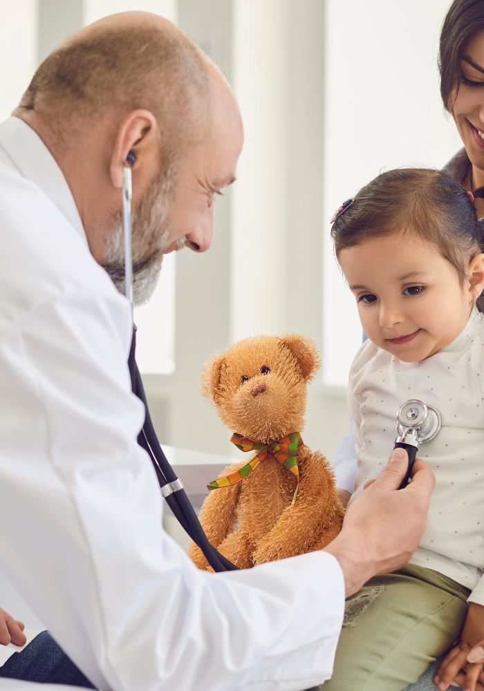 A doctor examining a child with a teddy bear.