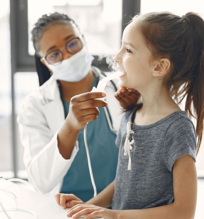 A woman in a white lab coat is helping a young girl with her breathing.