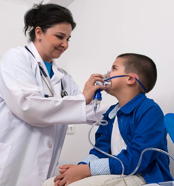 A woman in a white coat is helping a young boy with his breathing machine.