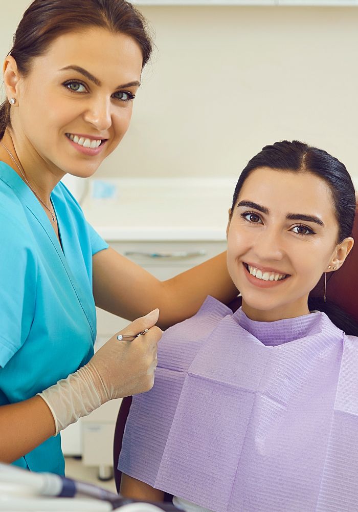 A woman in a blue shirt is smiling while a dentist works on her teeth.