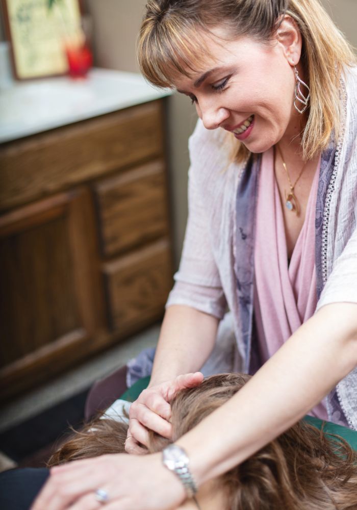 A woman with blonde hair is smiling and touching a person's head.