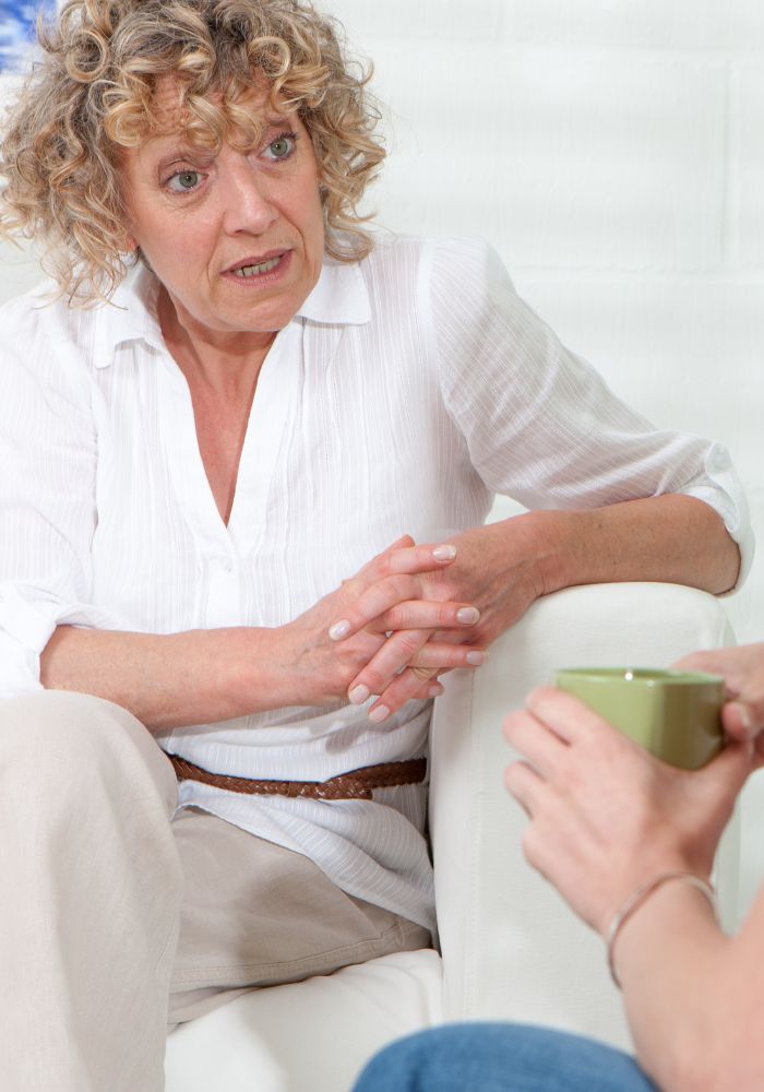 A woman with blonde hair and a white shirt sitting on a couch.