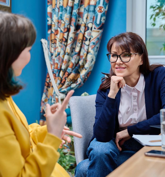 A woman wearing glasses and a blue sweater is sitting down.
