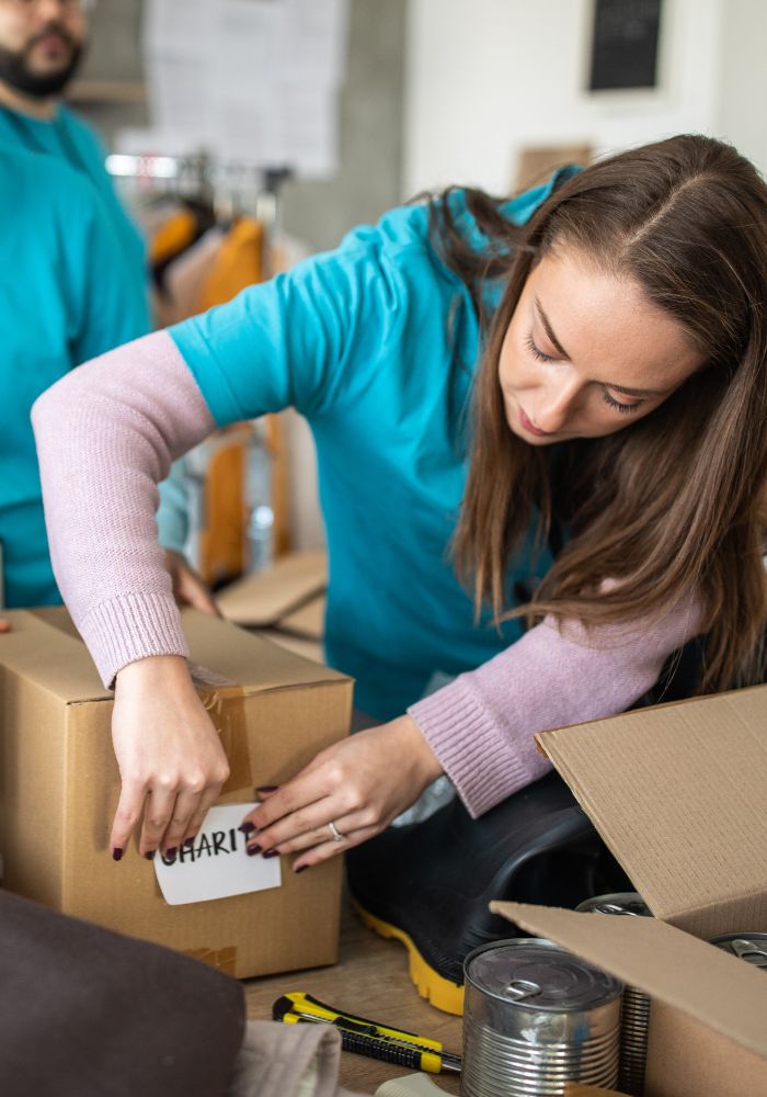 A woman in a blue shirt is opening a box that says "charity".